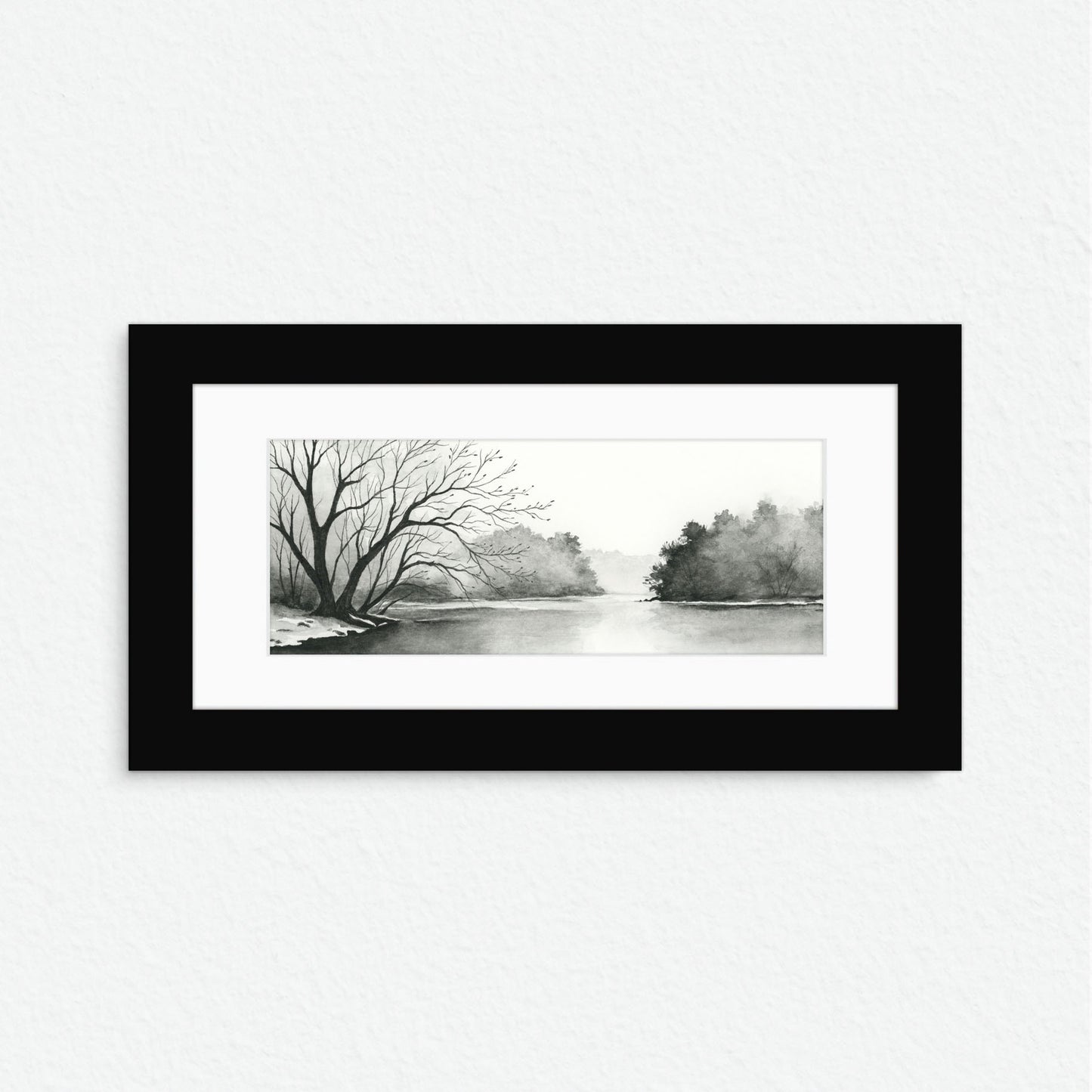 Framed black and white landscape print of a tree-lined river on a white wall.