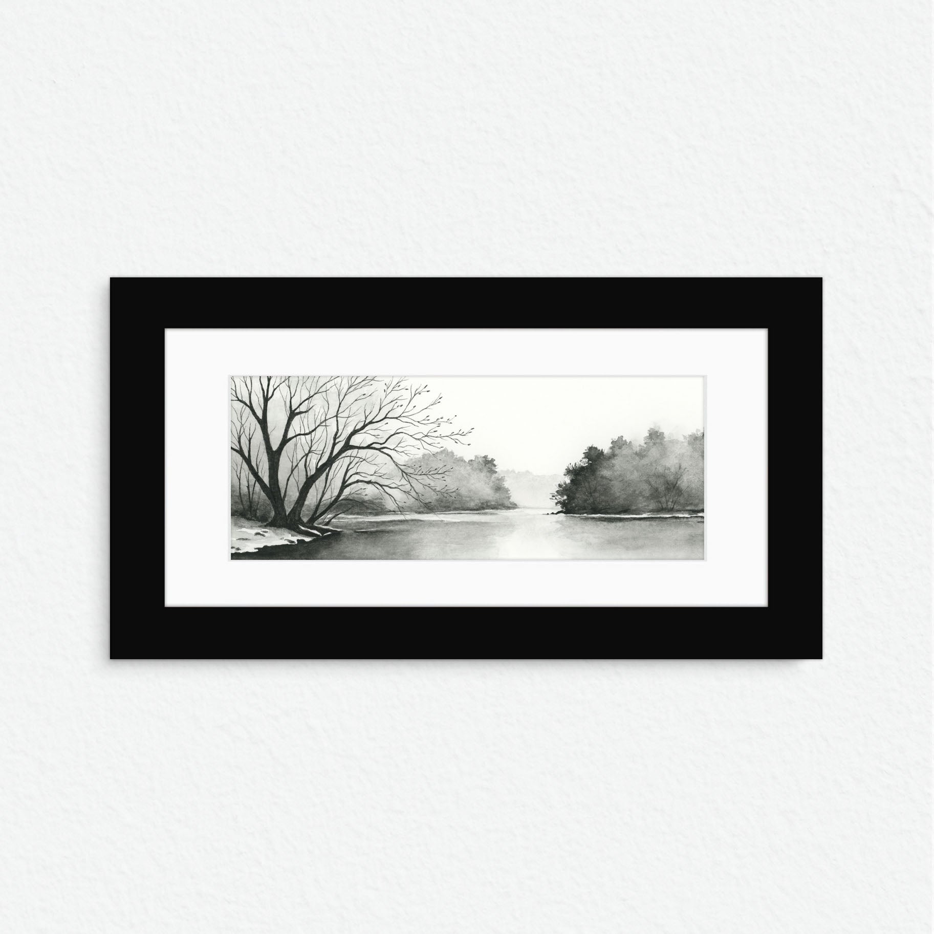 Framed black and white landscape print of a tree-lined river on a white wall.
